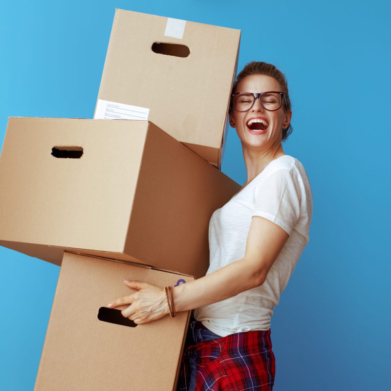 happy young woman holding pile of cardboard boxes on blue happy young woman in white t-shirt holding pile of cardboard boxes isolated on blue